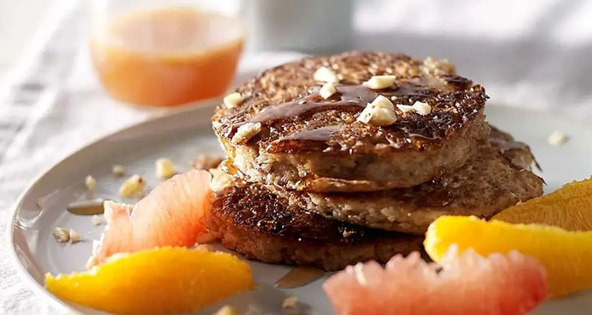 Pile de pancakes muesli, nappés de sirop et garnis de noix, accompagnés de quartiers d'agrumes.