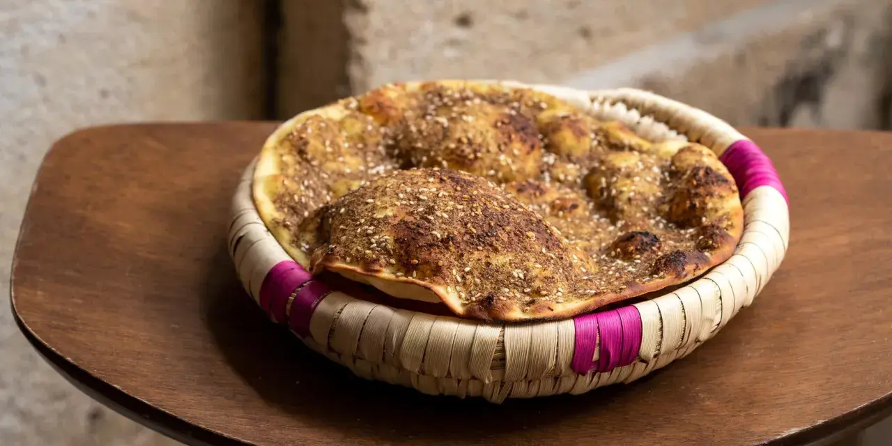 Manouche au zaatar, un délice croustillant aux épices, servi dans un panier tressé aux accents fuchsia.