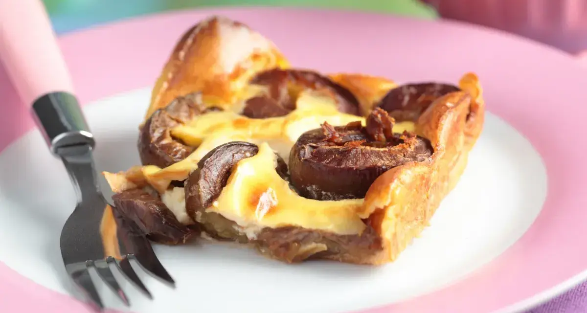 Tranche de clafoutis aux prunes moelleux sur une assiette rose avec une fourchette.