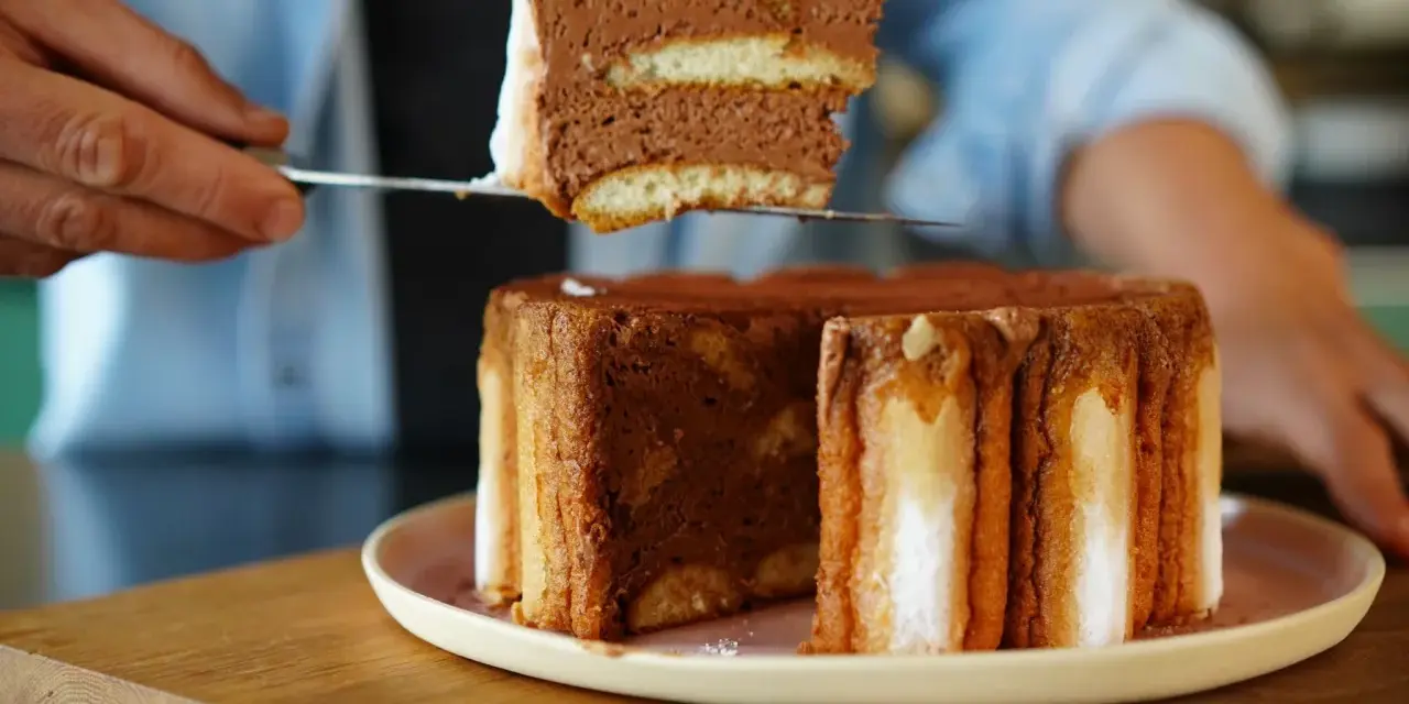 Une part de charlotte tiramisu, aérienne et chocolatée, est prélevée d'un gâteau entier.