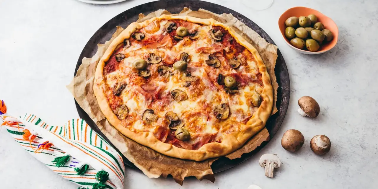 Une délicieuse pizza reine, garnie de jambon, champignons et olives, prête à être dégustée.