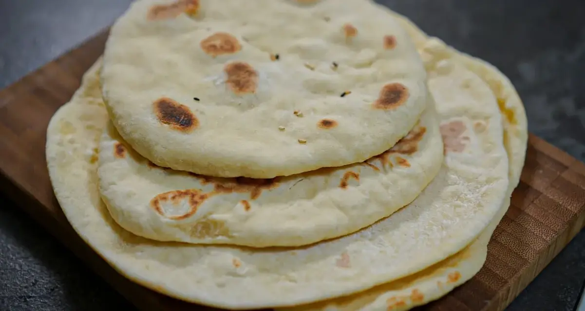 Pile de pains arabes moelleux, légèrement dorés par la cuisson, sur une planche en bois. Parfait pour accompagner un repas.