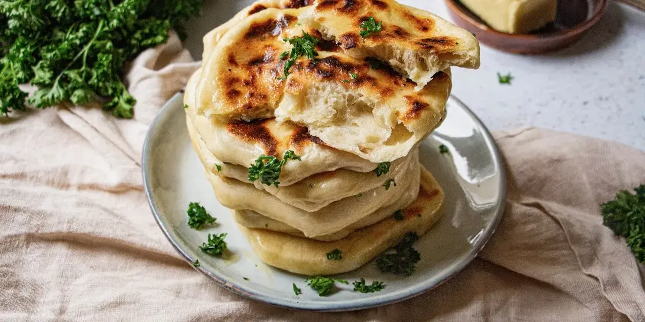 Pile de cheese naan moelleux, dorés et parsemés de persil frais. Un délice à déguster avec du beurre.