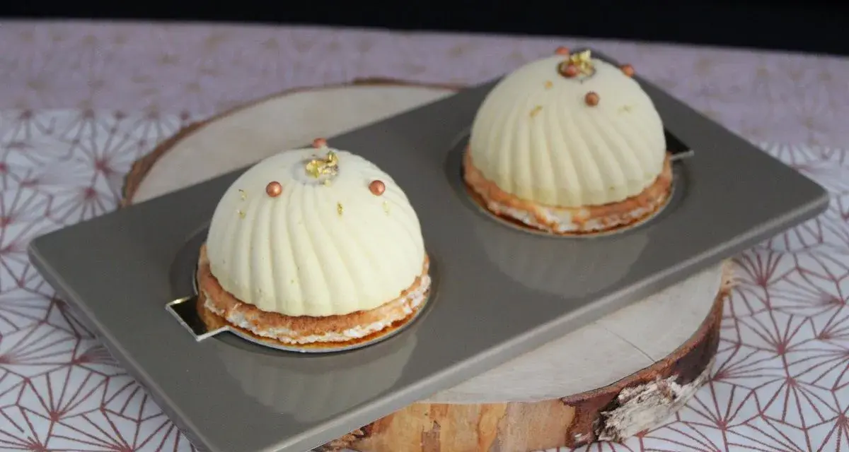 Deux dômes de dessert fruités, ornés de perles cuivrées et de feuilles d'or, reposent sur un plateau gris.