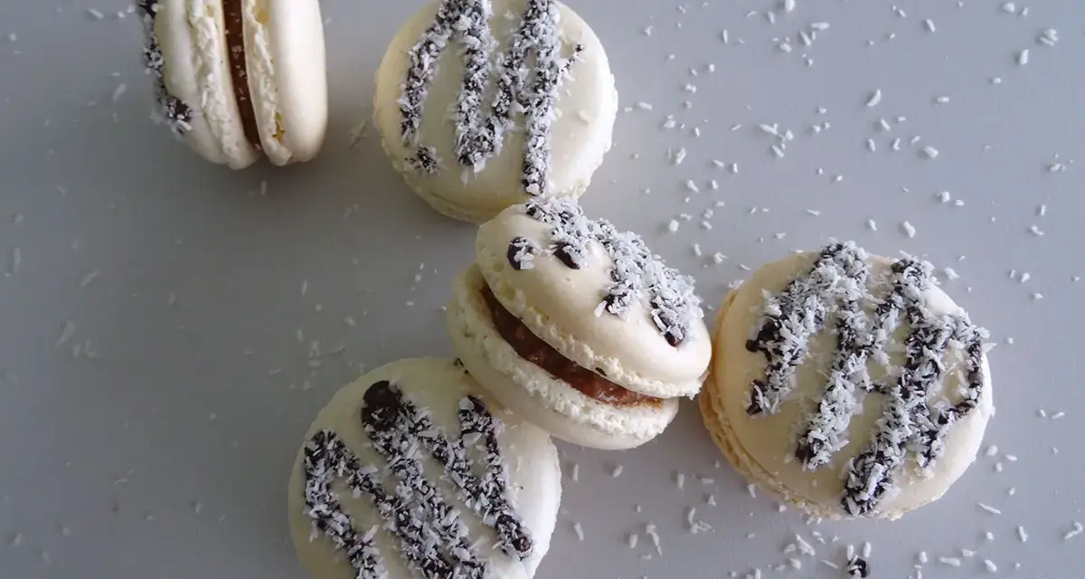 Macarons à la ganache coco, parsemés de noix de coco râpée et de copeaux de chocolat noir.