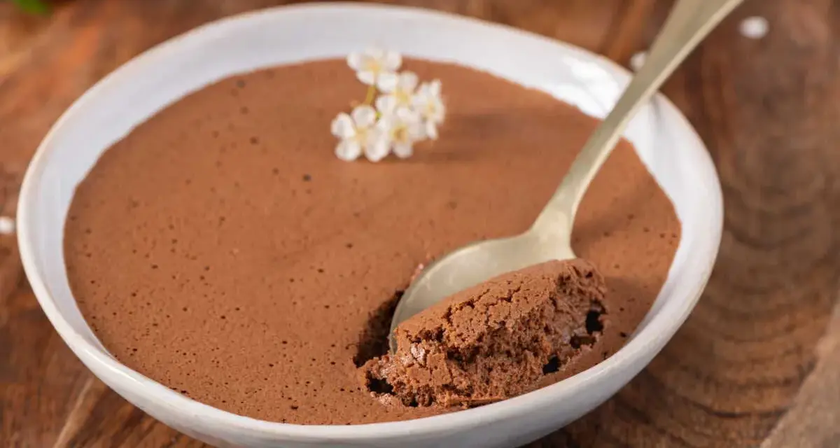 Une cuillère prend une bouchée d'une mousse au chocolat au lait aérienne, décorée de petites fleurs blanches.