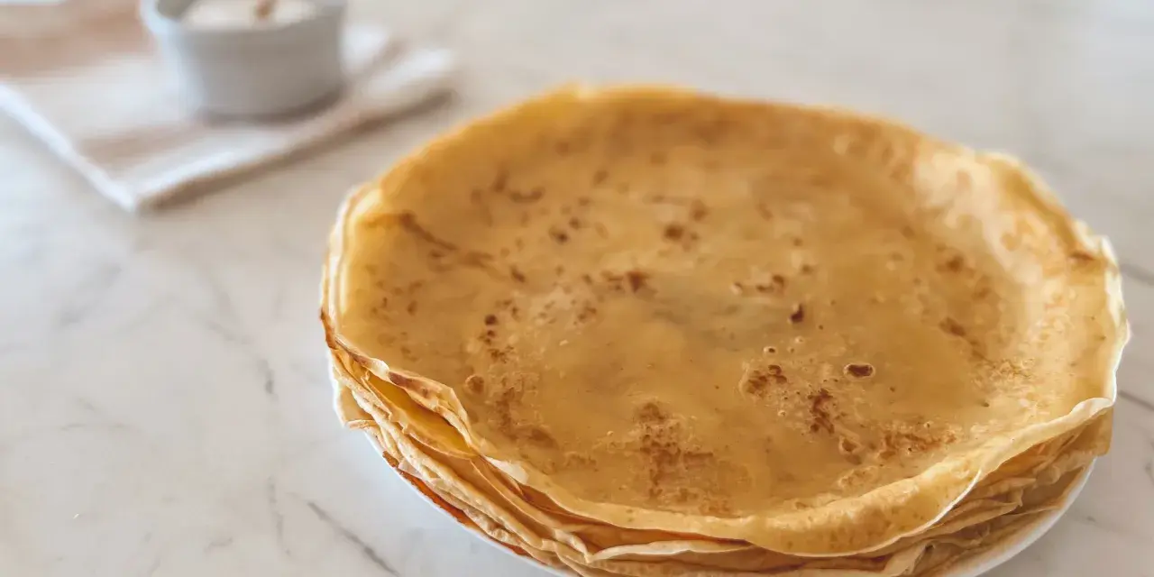 Pile de crêpes dorées, parfaites pour une recette crêpe moelleuse. Un petit bol de sucre est à côté.