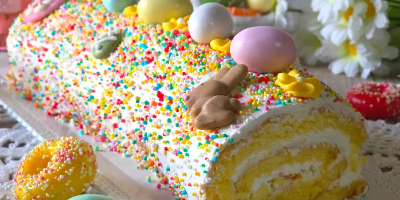 Bûche roulée décorée pour Pâques, recouverte d'un glaçage mascarpone facile et de vermicelles colorés, avec des œufs et un lapin en chocolat.