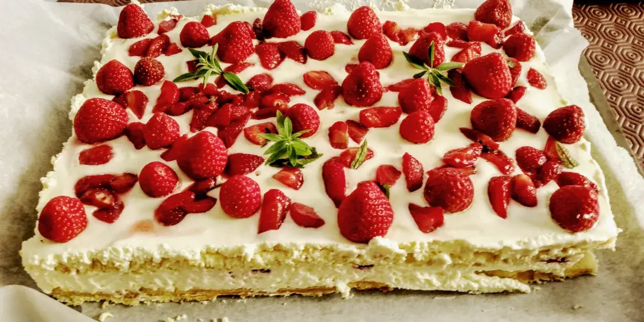 Un délicieux entremet fraise, garni de fruits rouges frais et de feuilles de menthe, sur une base crémeuse.
