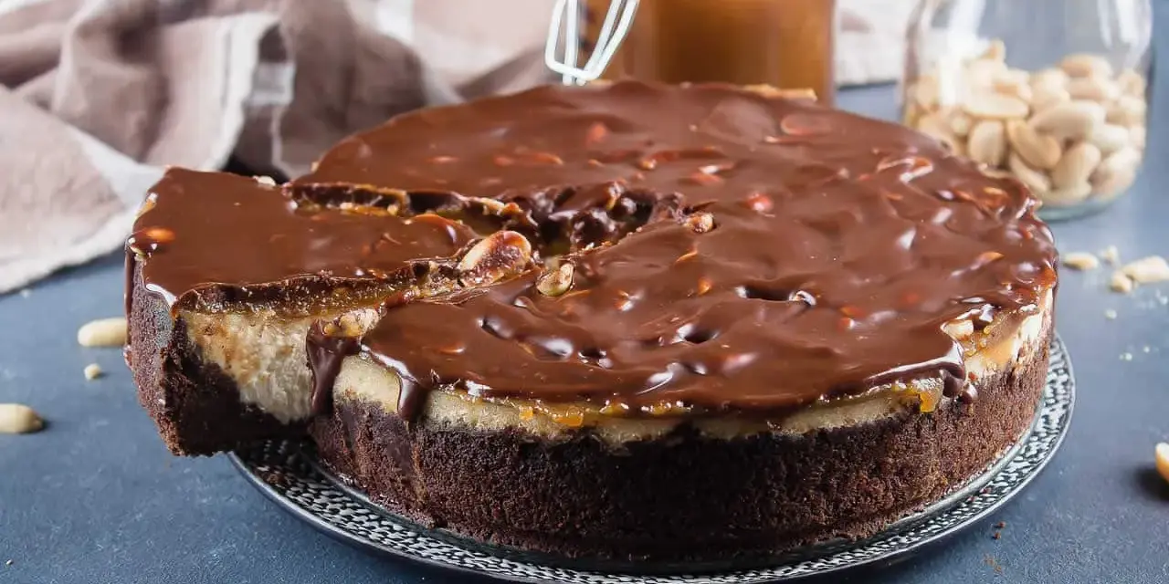 Gâteau façon Snickers, avec une base chocolatée, une couche crémeuse, du caramel coulant et une ganache au chocolat parsemée de cacahuètes. Un délice !