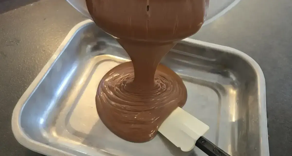 Une ganache au chocolat, inspirée par le Toblerone, est versée dans un plat métallique. Une spatule aide à l'étaler.