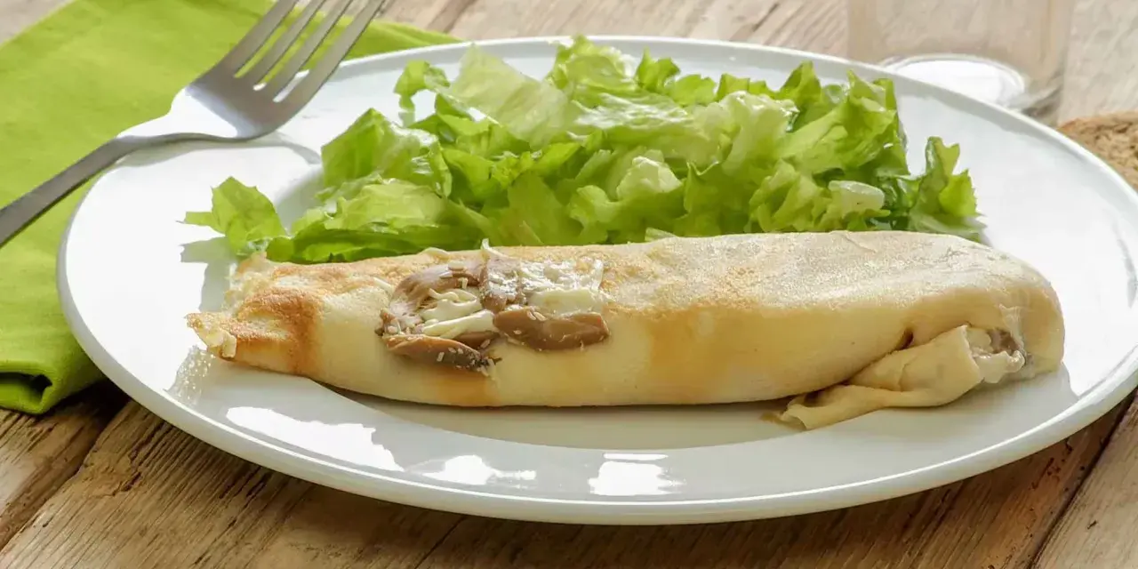 Une ficelle picarde garnie de champignons et de fromage, accompagnée d'une salade verte croquante sur une assiette blanche.
