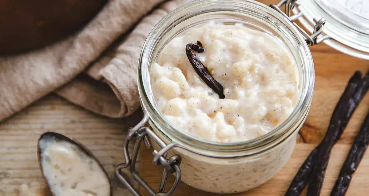 Un pot en verre rempli de riz au lait au four, garni d'une gousse de vanille. Une cuillère à côté en témoigne.