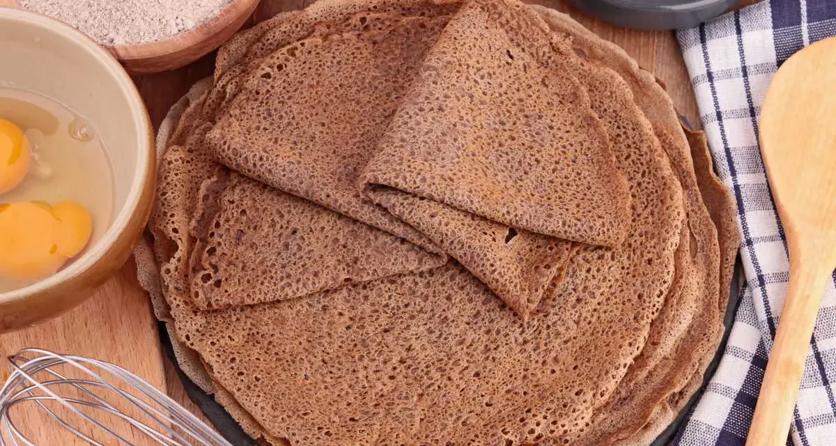 Pile de crêpes de sarrasin, avec des ingrédients pour la pâte à crêpe sarrasin : farine, œufs, beurre.