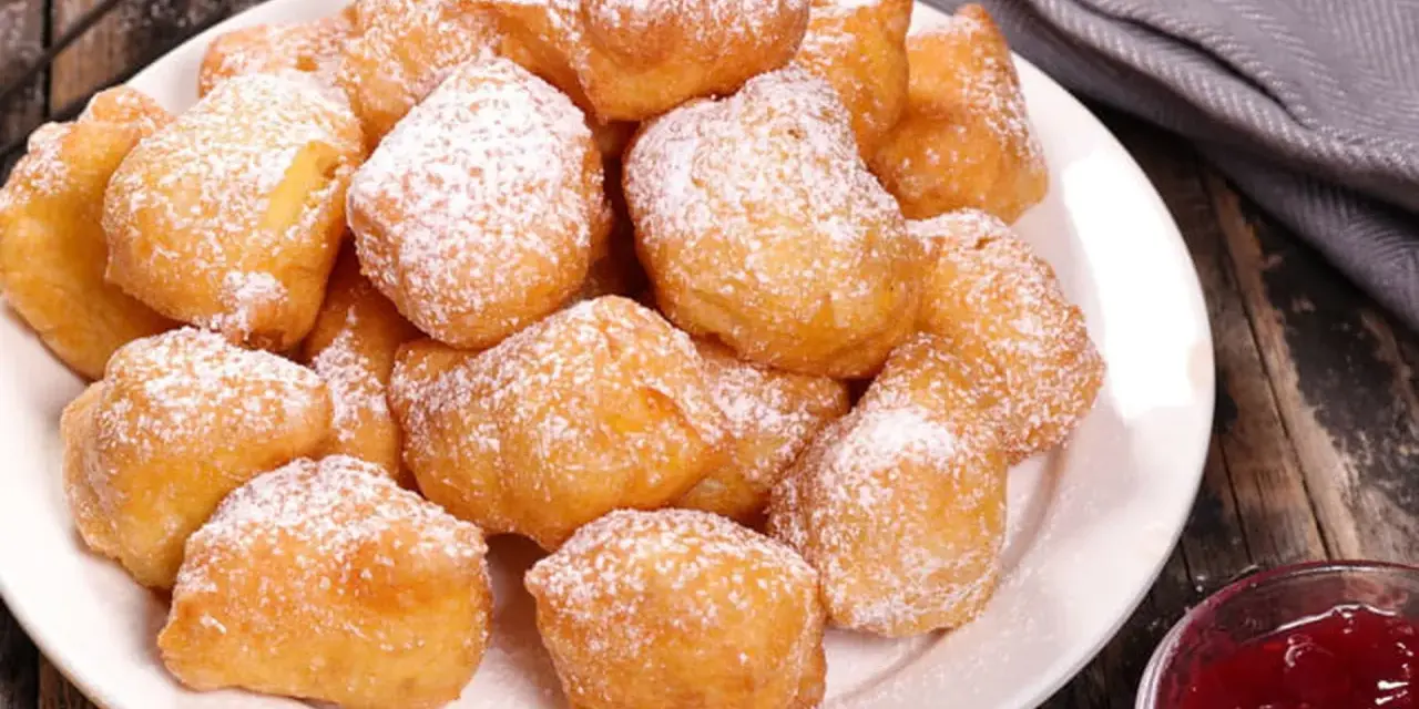 Une assiette de beignets banane saupoudrés de sucre glace, prêts à être dégustés avec une confiture de fruits rouges.