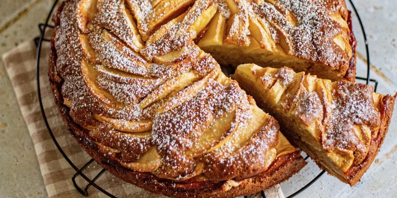 Gâteau mascarpone pommes, une tranche coupée, saupoudré de sucre glace. Un délice doré et moelleux.