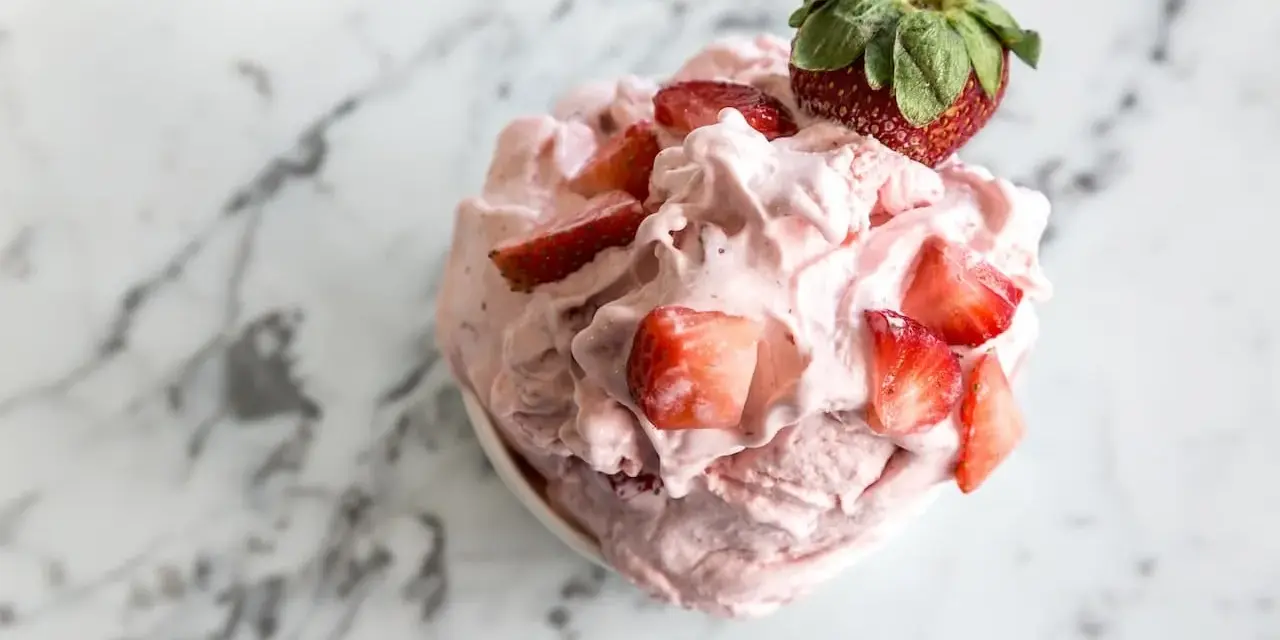 Un délice rose et crémeux : un sorbet fraise garni de morceaux de fruits frais et d'une fraise entière sur un fond marbré.