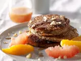 Pile de pancakes muesli, nappés de sirop et garnis de noix, accompagnés de quartiers d'agrumes.