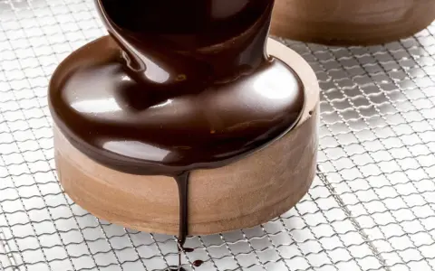 Un glaçage chocolat brillant et onctueux recouvre un petit gâteau rond, coulant sur les côtés.