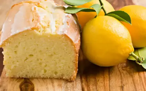 Un délicieux gâteau citron, avec un glaçage blanc et des citrons frais sur une planche en bois.