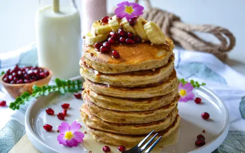 Pile de pancake banane avoine, garnie de fruits rouges, de rondelles de banane et de fleurs roses. Un délice matinal !