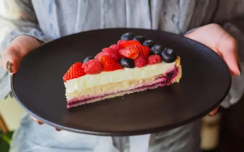 Tranche de tarte aux fruits rouges sur une crème mousseline onctueuse, présentée sur une assiette noire.