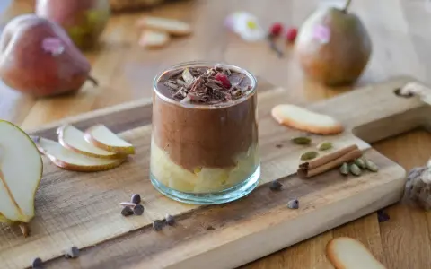 Délicieuse recette mousse poire chocolat, garnie de copeaux de chocolat et d'une framboise. Poires fraîches et épices sur fond de bois.