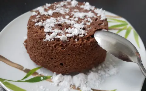 Un délicieux bowl cake au chocolat, saupoudré de sucre glace, prêt à être dégusté avec une cuillère.