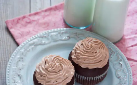 Deux cupcakes au chocolat avec une ganache chocolat passion onctueuse, servis sur une assiette bleue avec deux verres de lait.