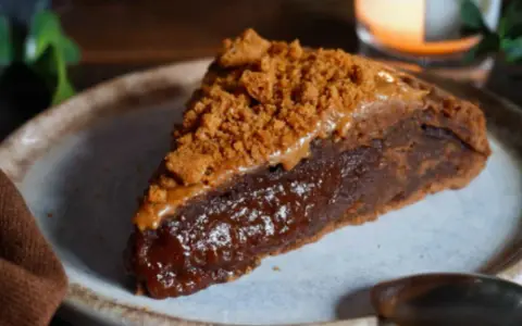 Une part de gâteau speculoos, riche et gourmande, garnie de miettes de biscuits et d'une sauce caramel.