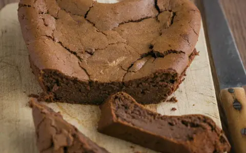 Un délicieux gâteau au chocolat en forme de cœur, un gâteau sans oeuf, craquelé sur le dessus, avec une part coupée.