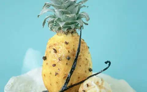 Un ananas rôti, parsemé de clous de girofle et de gousses de vanille, sur un fond bleu pâle. Un délice sucré et épicé.
