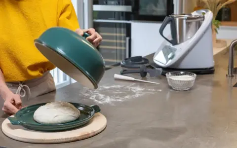 Préparation de la pâte à pizza avec un robot culinaire. Une boule de pâte repose sur un plat vert, prête à être cuite.