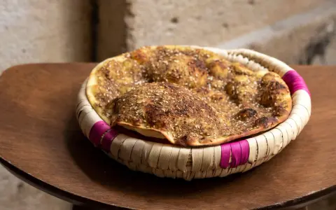 Manouche au zaatar, un délice croustillant aux épices, servi dans un panier tressé aux accents fuchsia.