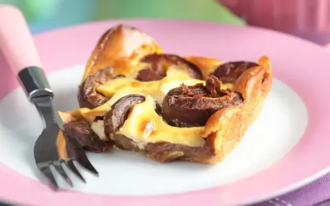 Tranche de clafoutis aux prunes moelleux sur une assiette rose avec une fourchette.