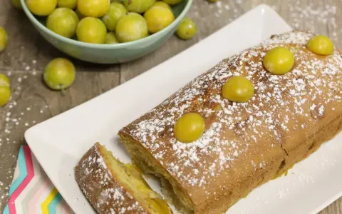 Gâteau lorrain aux mirabelles, saupoudré de sucre glace, avec des mirabelles fraîches sur le dessus et dans une coupelle à côté.