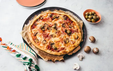 Une délicieuse pizza reine, garnie de jambon, champignons et olives, prête à être dégustée.