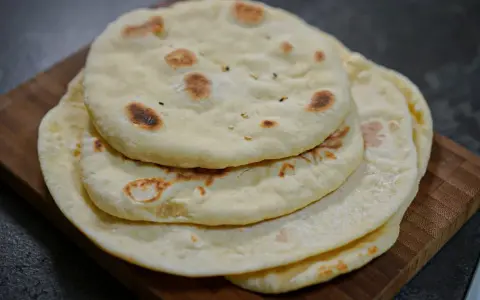 Pile de pains arabes moelleux, légèrement dorés par la cuisson, sur une planche en bois. Parfait pour accompagner un repas.
