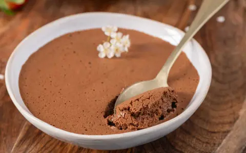Une cuillère prend une bouchée d'une mousse au chocolat au lait aérienne, décorée de petites fleurs blanches.