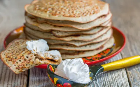 Pile de crêpes épaisses alsaciennes, garnies de crème fraîche. Une cuillère décorée en est aussi remplie.