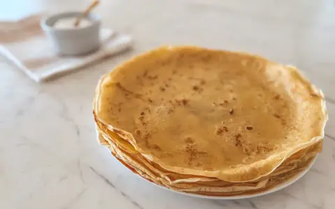 Pile de crêpes dorées, parfaites pour une recette crêpe moelleuse. Un petit bol de sucre est à côté.