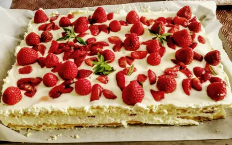 Un délicieux entremet fraise, garni de fruits rouges frais et de feuilles de menthe, sur une base crémeuse.