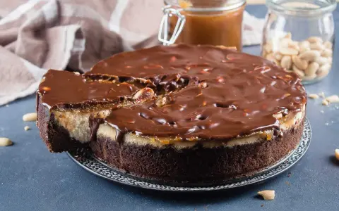 Gâteau façon Snickers, avec une base chocolatée, une couche crémeuse, du caramel coulant et une ganache au chocolat parsemée de cacahuètes. Un délice !