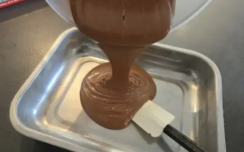 Une ganache au chocolat, inspirée par le Toblerone, est versée dans un plat métallique. Une spatule aide à l'étaler.