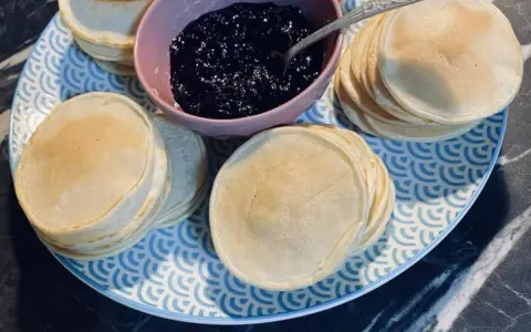 Une assiette bleue et blanche présente des piles de poffertjes dorés, accompagnés d'un bol de confiture de myrtilles. Parfait pour une recette de poffertjes !