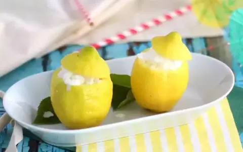 Deux citrons évidés remplis de sorbet citron, servis sur une assiette blanche, avec des feuilles vertes et des pailles colorées en arrière-plan.