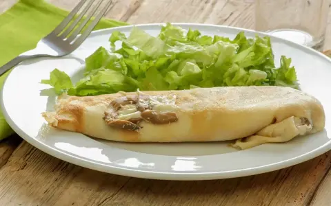 Une ficelle picarde garnie de champignons et de fromage, accompagnée d'une salade verte croquante sur une assiette blanche.