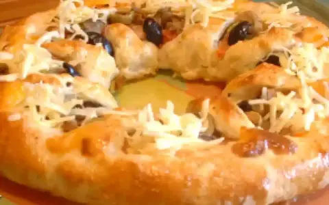 Pizza maison avec une croûte dorée, garnie d'olives noires et de fromage râpé. Parfait pour une recette pâte à pizza rapide.