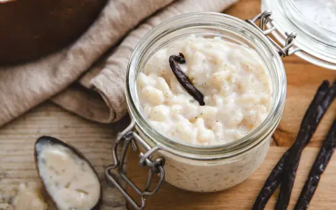 Un pot en verre rempli de riz au lait au four, garni d'une gousse de vanille. Une cuillère à côté en témoigne.