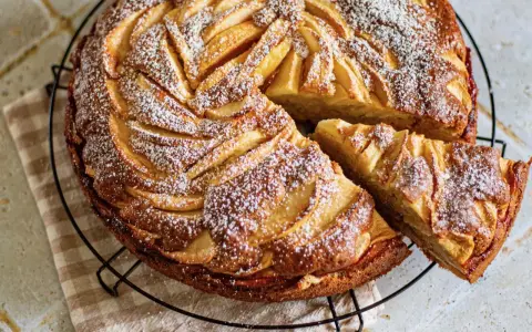 Gâteau mascarpone pommes, une tranche coupée, saupoudré de sucre glace. Un délice doré et moelleux.
